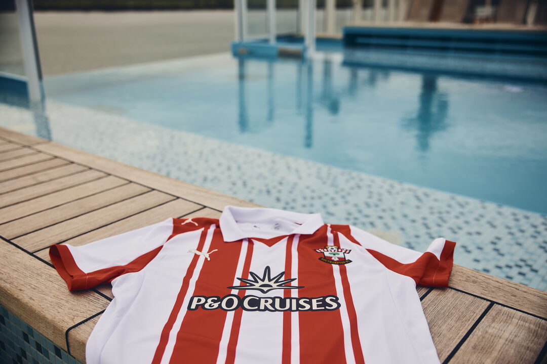 A red and white striped Southampton football shirt with the P&O Cruises logo is laid out on a wooden decking next to a swimming pool with blue water.
