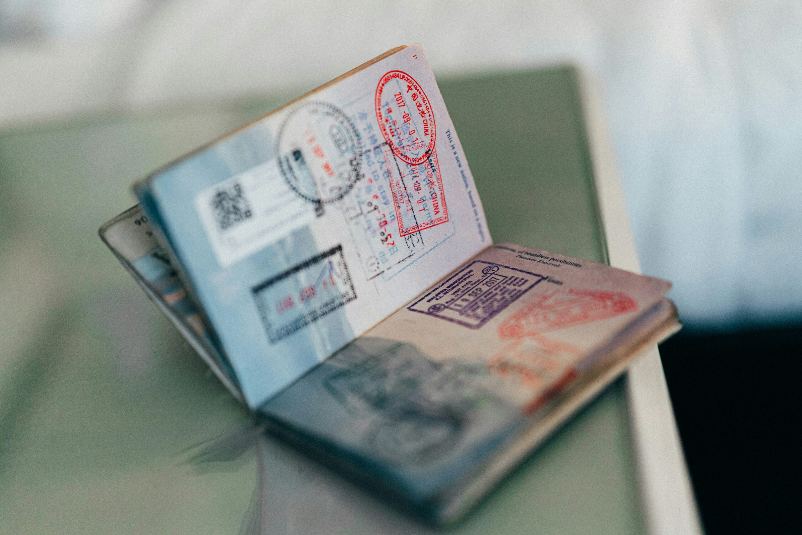 An open passport lies on a glass surface, showing multiple colourful entry and exit stamps from different countries on its pages.