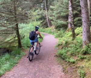 A person wearing a helmet and rucksack rides a bicycle on a dirt path through a lush, green forest.