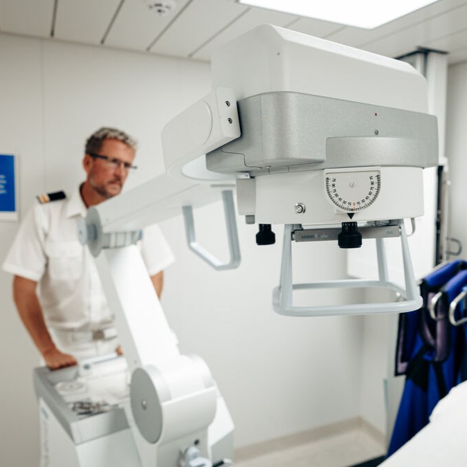 A man in a white uniform stands beside a large, modern medical imaging machine in a bright, clean room.