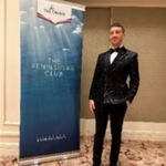 A person in a black, sparkly suit and bow tie stands next to a blue sign that reads The Peninsular Club in a formal indoor setting.