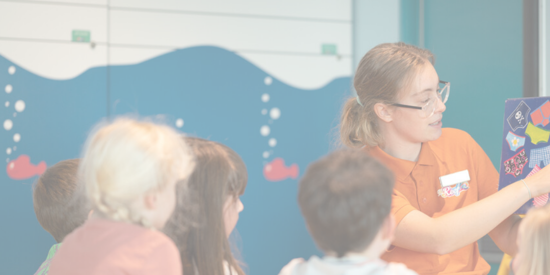 A teacher in an orange shirt shows children a board with underwear and a skull and crossbones.