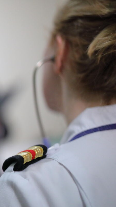 A person in uniform with epaulettes and red and gold stripes is seen from behind, wearing a stethoscope round their neck, suggesting a medical or healthcare professional.