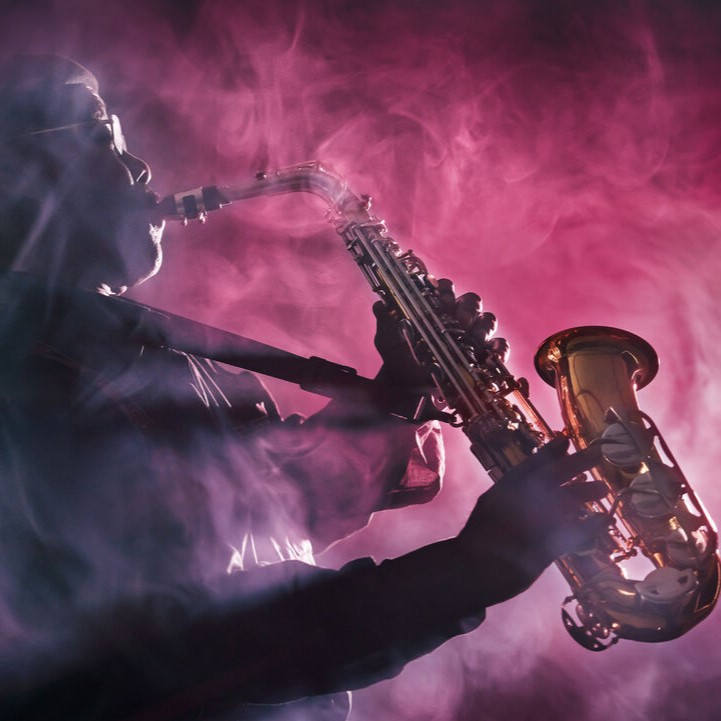 A person playing a saxophone is silhouetted against a background of swirling purple and pink smoke, creating a dramatic and atmospheric scene.