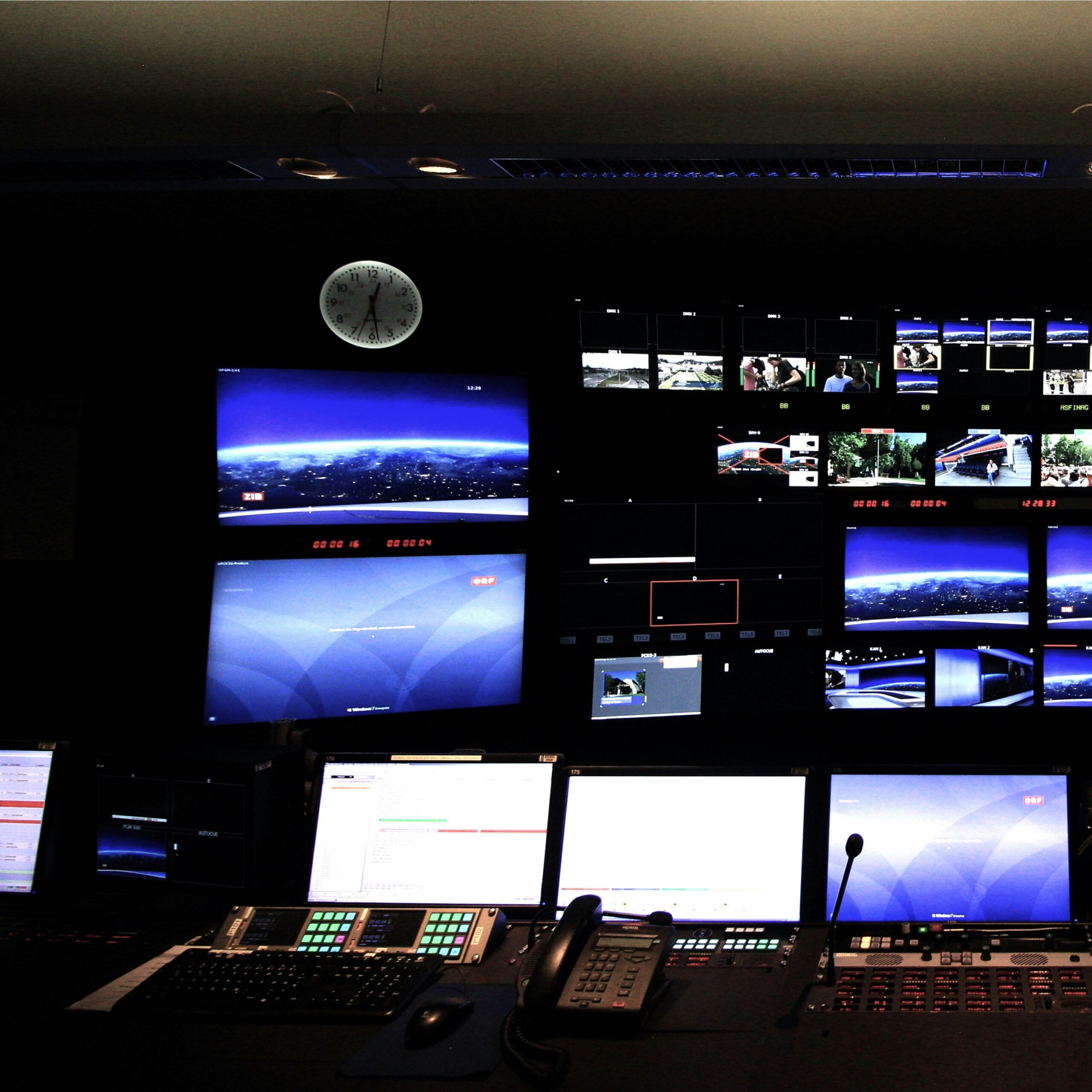 A dimly lit control room with multiple computer monitors, control panels, and large wall screens displays various broadcast feeds; a clock showing 9:17 hangs above the screens, evoking the behind-the-scenes precision of P&O Cruises technical careers.