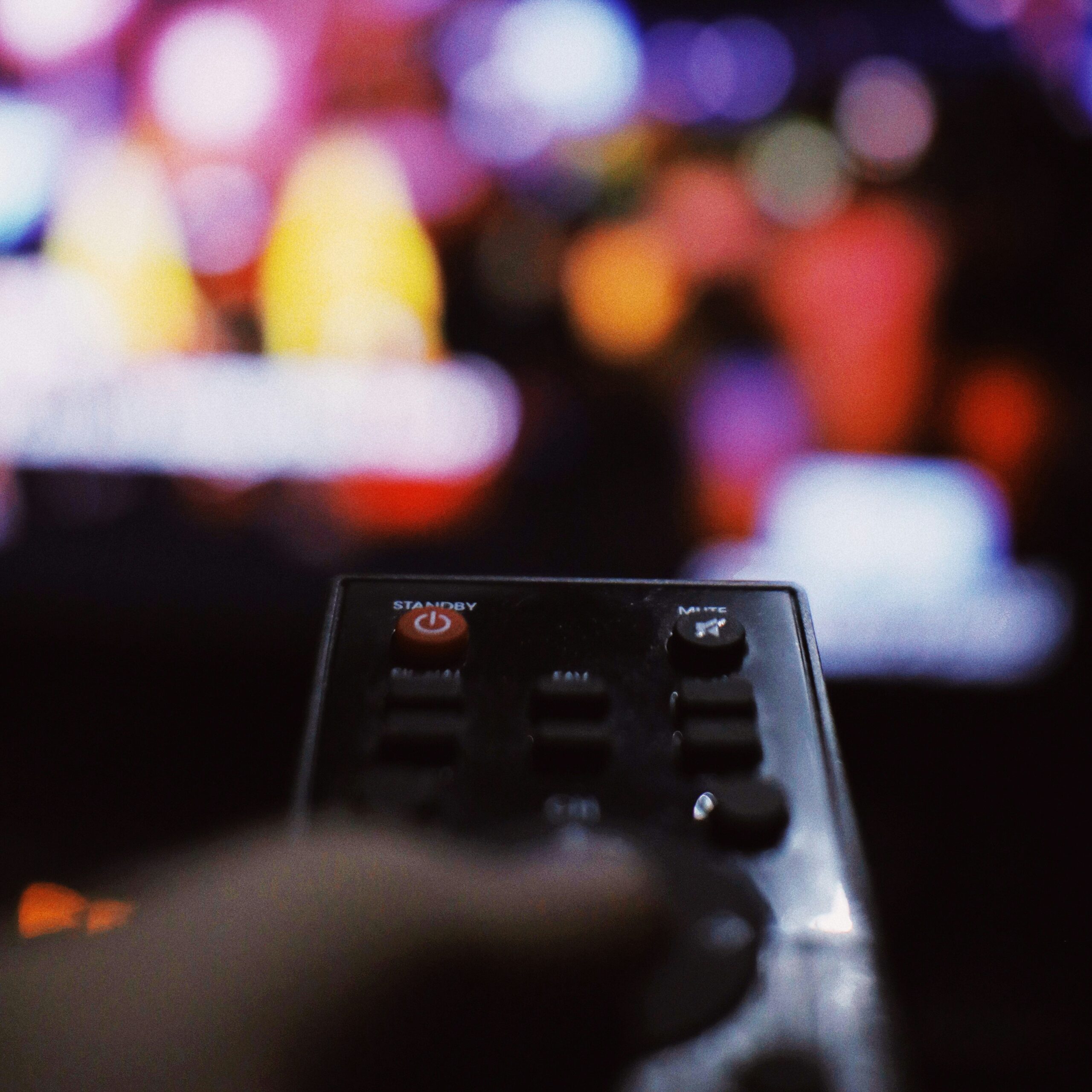 A close-up of a hand holding a TV remote, pointed at a blurred, colourful television screen in the background. Perfect for illustrating focus and control—much like P&O Cruises technical careers behind the scenes.