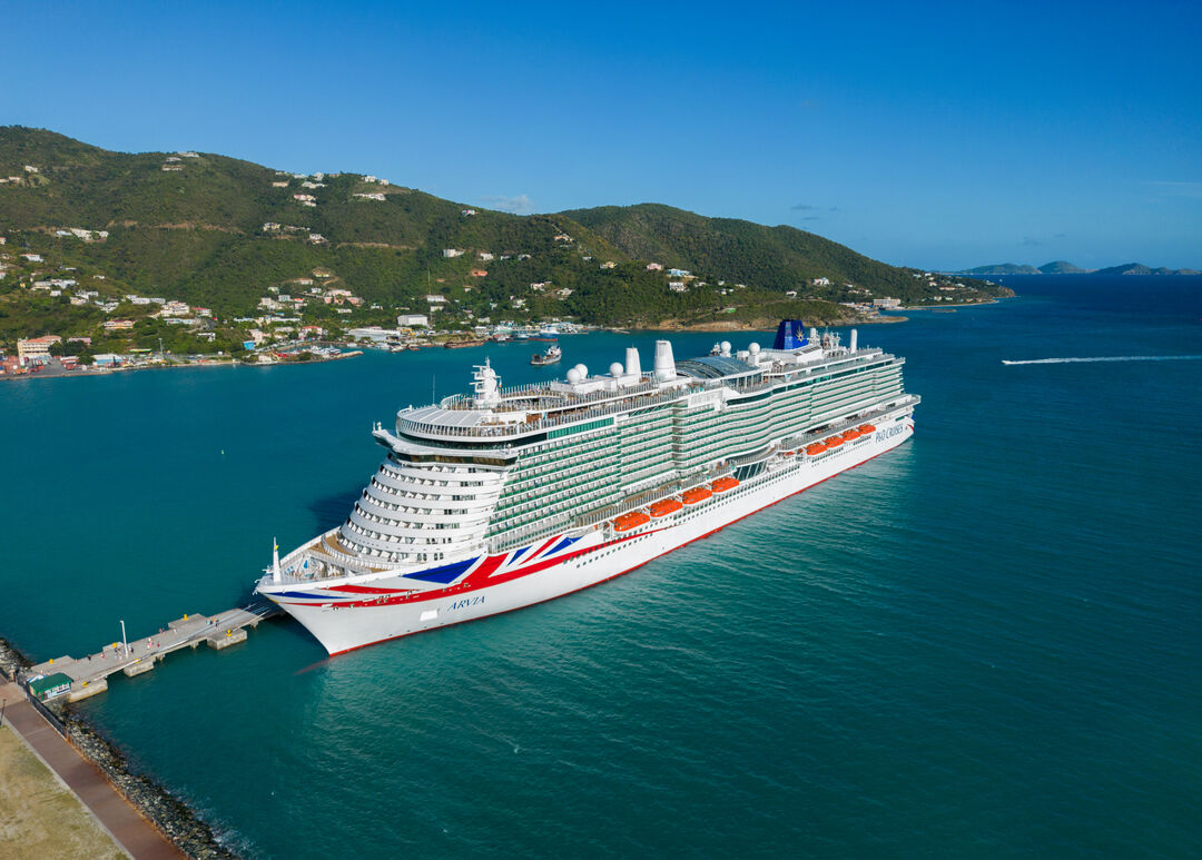 A large white P&O Cruises ship berthed at a pier in clear blue water, with green hills and scattered houses in the background—an inspiring scene for those interested in technical careers at sea under a bright blue sky.