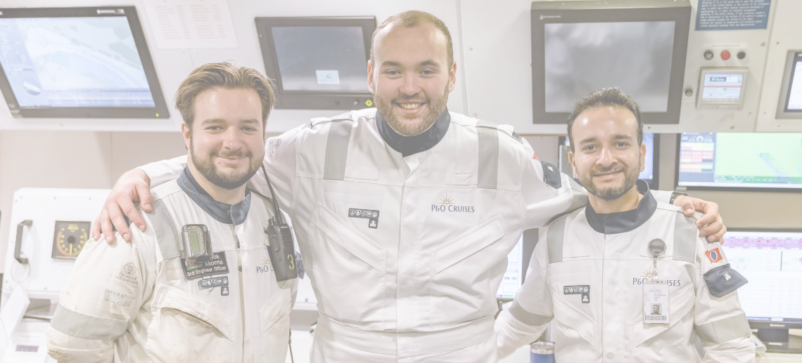 Three crew members in white P&O Cruises uniforms stand together smiling, with their arms round each other, inside a ship’s control room—highlighting the teamwork and expertise found in P&O Cruises technical careers.