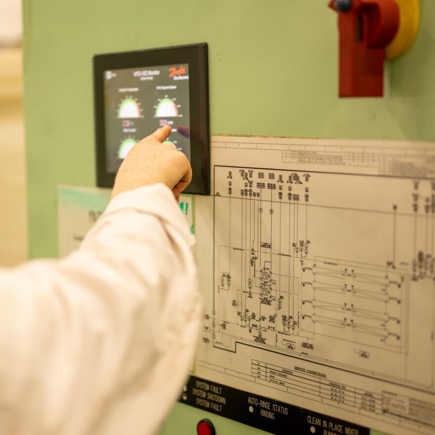 A person in a white lab coat is touching a touchscreen control panel on a machine, with an electrical schematic diagram and indicator lights—ideal for those interested in P&O Cruises technical careers.