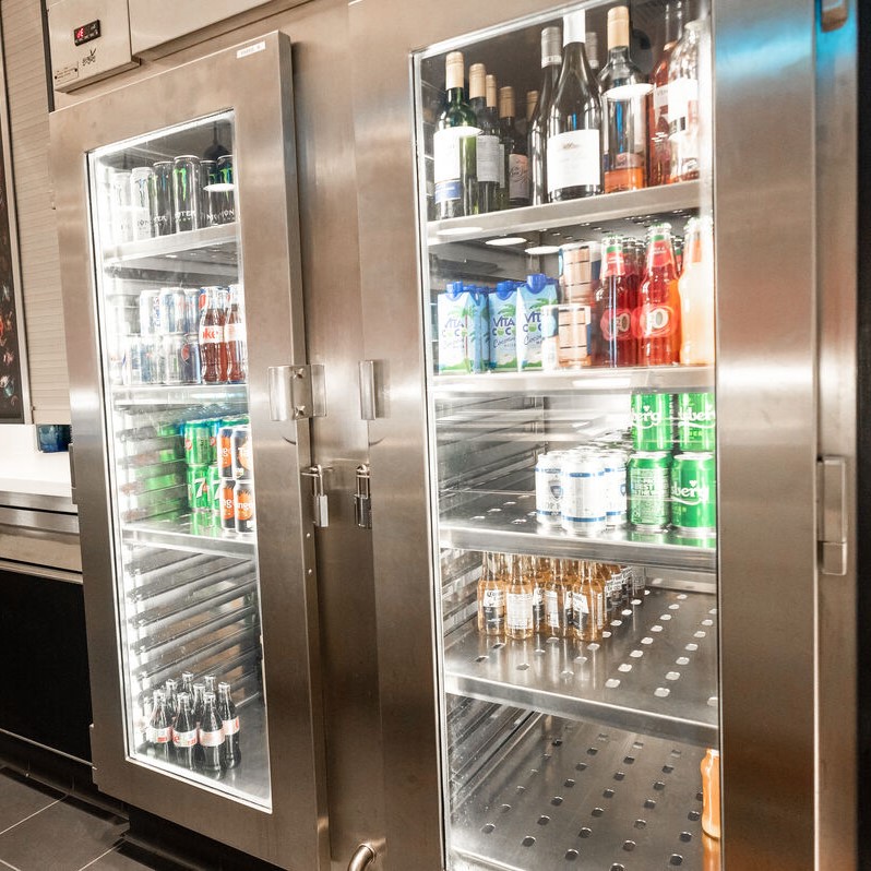 A glass-door fridge stocked with various beverages, including wine bottles, fizzy drink cans, bottled water, and other drinks—neatly arranged on metal shelves—reflects the order and precision valued in P&O Cruises technical careers.