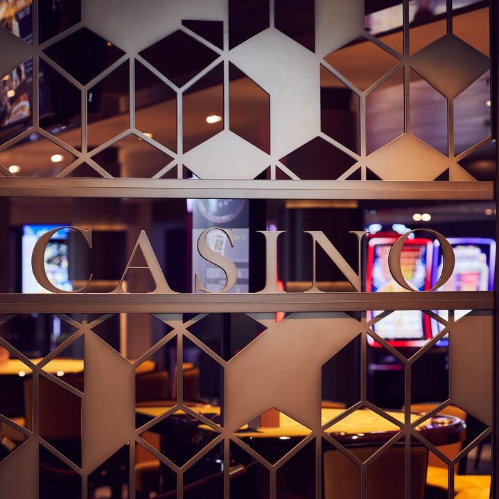 A decorative metal screen with geometric patterns displays the word CASINO in cut-out letters, with colourful fruit machines and warm lights visible in the background.