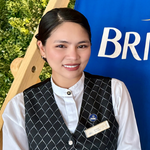 Crew member in formal attire standing in front of a blue branded P&O Cruises deckchair.