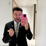 Crew member in formal attire taking a mirror selfie in a bright indoor space, holding a phone, with corridor lighting visible.