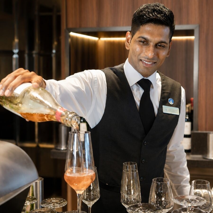 Wine bar host pouring rosé wine into glass at cruise ship bar, providing specialist drinks service and guest experience