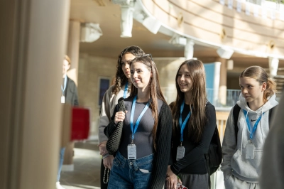 Younger individuals standing side by side indoors, wearing lanyards, in a warmly lit space with wooden and glass features
