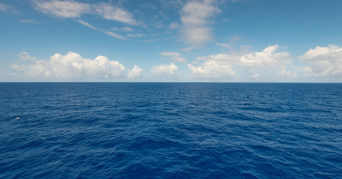 Wide view of open ocean under a blue sky with scattered clouds, showing calm water stretching to the horizon.