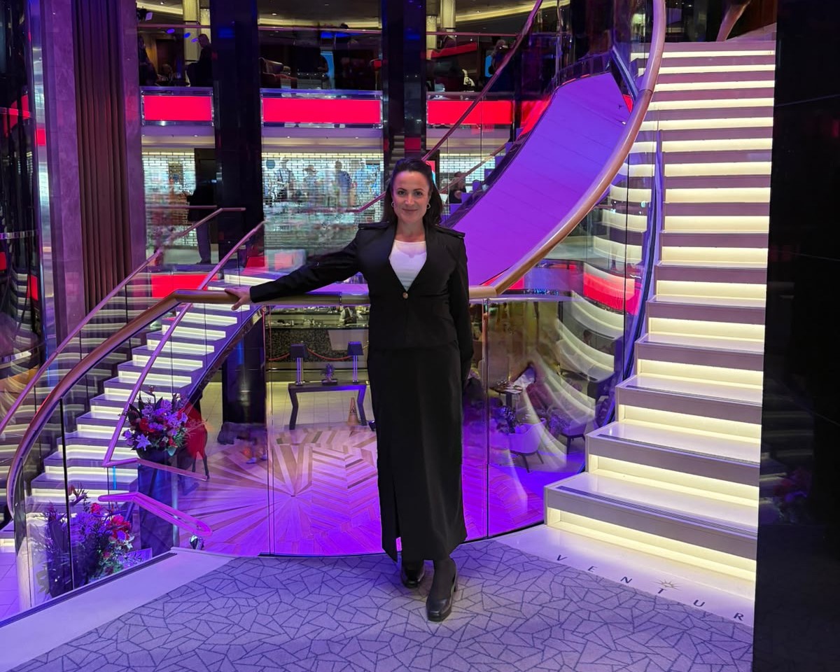 Carnival UK cadet in professional uniform standing on a grand staircase onboard a cruise ship, with modern lighting and open atrium design, representing award‑winning early careers talent.