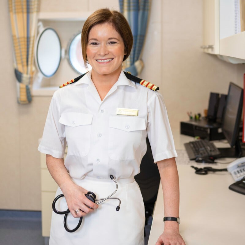 Senior medical professional in P&O Cruises uniform standing in the ship's medical centre with a stethoscope. The image highlights healthcare careers at sea, onboard medical facilities, crew wellbeing, and opportunities for doctors and medical professionals working on P&O Cruises ships.