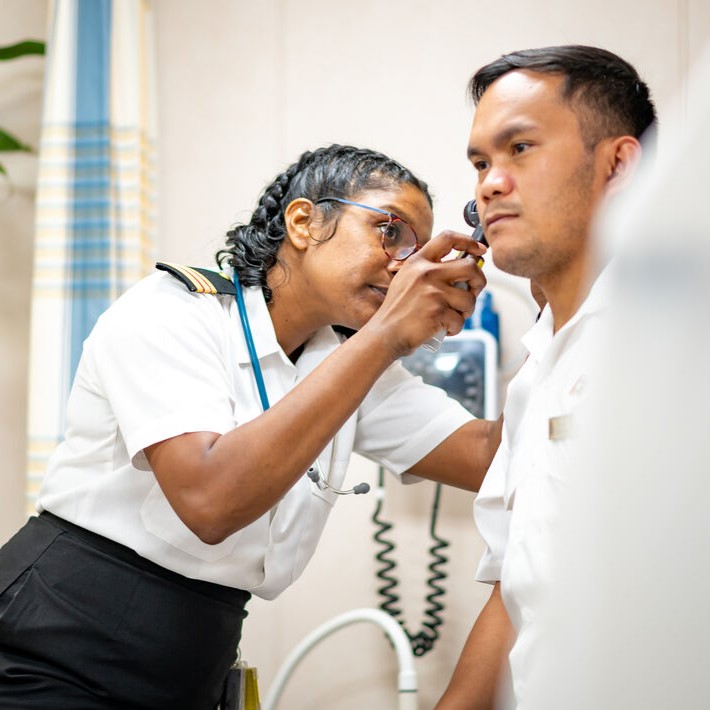 Senior medical professional in P&O Cruises uniform standing in the ship's medical centre with a stethoscope. The image highlights healthcare careers at sea, onboard medical facilities, crew wellbeing, and opportunities for doctors and medical professionals working on P&O Cruises ships.
