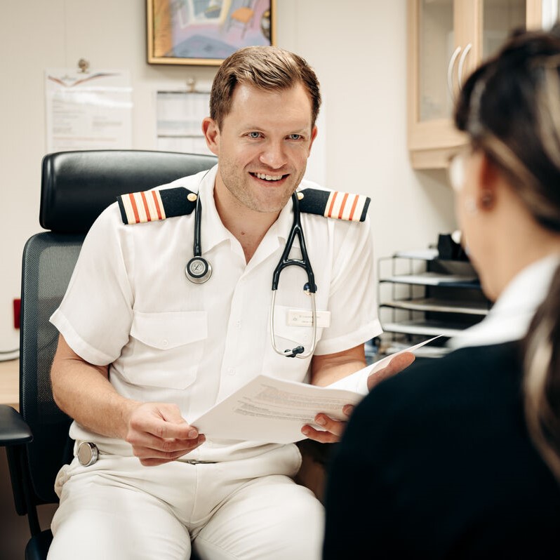 Senior doctor in the P&O Cruises onboard medical centre reviewing healthcare documents during a crew consultation. The image highlights maritime medical careers, onboard healthcare services, crew wellbeing, and opportunities for doctors working at sea with P&O Cruises.
