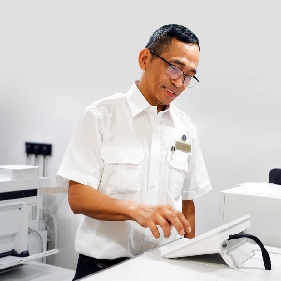 Crew member working in the onboard print room aboard a P&O Cruises ship, using print management equipment to produce operational and guest communications materials. The image highlights administrative, office support and communications careers at sea within the cruise industry.