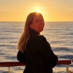 A ship's nurse stands on a ship’s deck at sunset, looking towards the camera. The golden light sets a tranquil scene—perfect for those interested in Cruise Ship Nurse Jobs and life at sea. A life buoy and railing are visible.