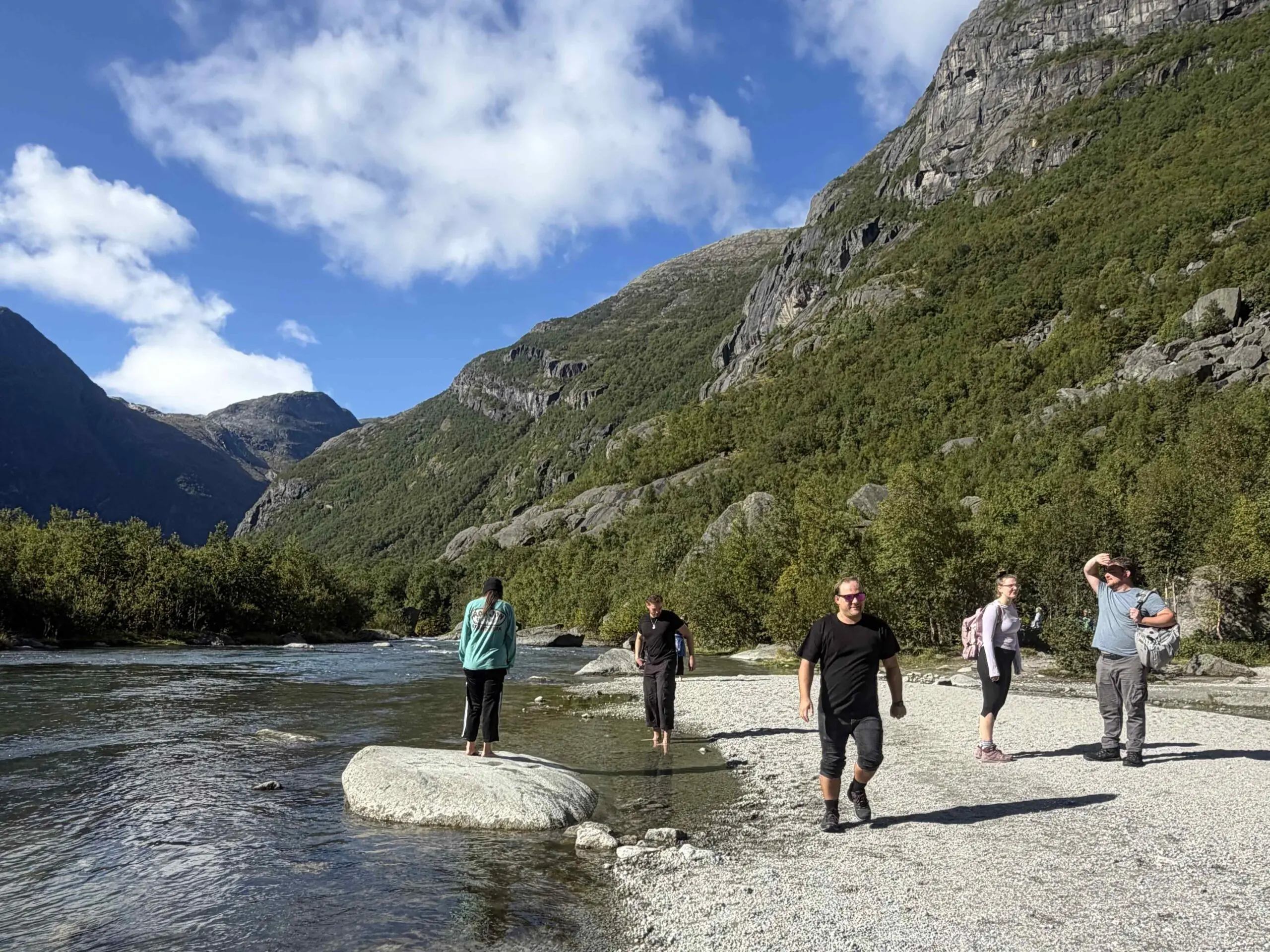 Arvia crew members explore a riverside trail in Norway, surrounded by dramatic mountains, forests and clear glacial water.